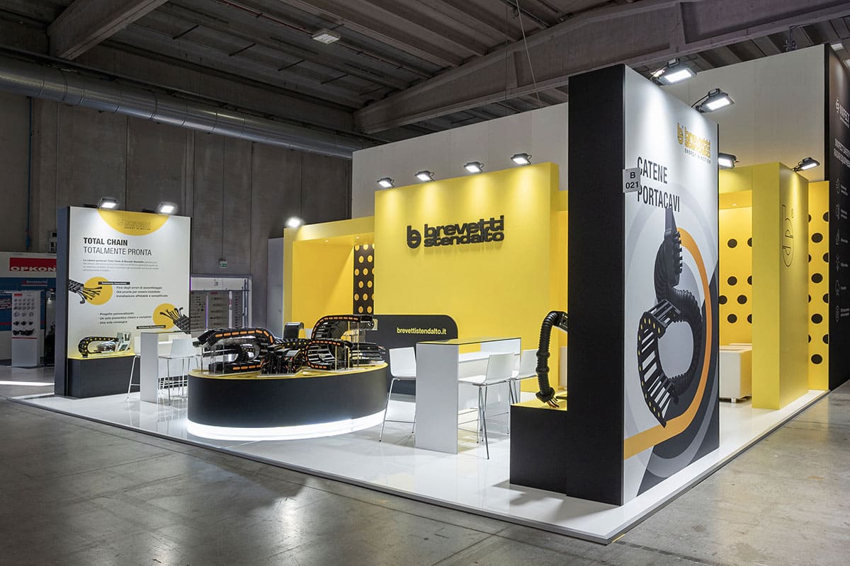 Allestimenti fieristici SPS Parma ed SPS Norimberga casi reali: l'allestimento stand realizzato per Brevetti Stendalto L'immagine raffigura un caso reale di allestimento fieristico: l'allestimento dello stand Brevetti Stendalto realizzato da Diquadro in occasione di due precedenti edizioni delle fiere Sps di Parma ed Sps di Norimberga. La foto mostra una panoramica dell'allestimento dello stand visto da Sud Est. In particolare, mostra il blocco espositivo laterale ad Ovest e quello centrale di forma circolare con base retroilluminata.
