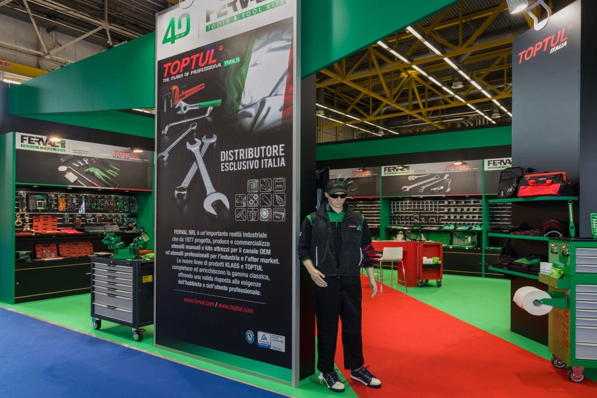 L'immagine raffigura un caso reale di allestimento fieristico: l'allestimento dello stand Ferval realizzato da Diquadro in occasione di una precedente edizione della fiera Autopromotec di Bologna. In particoalre, nella foto si vede la fiancata Est dello stand con panoramica sull'ingresso principale.