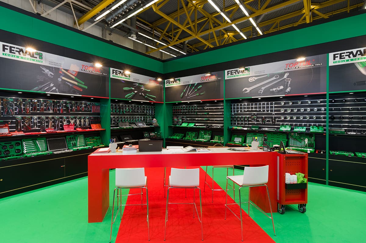 L'immagine raffigura un caso reale di allestimento fieristico: l'allestimento dello stand Ferval realizzato da Diquadro in occasione di una precedente edizione della fiera Autopromotec di Bologna. L'immagine mostra la zona centrale dello stand dove campeggia il grande tavolo alto retroilluminato.
