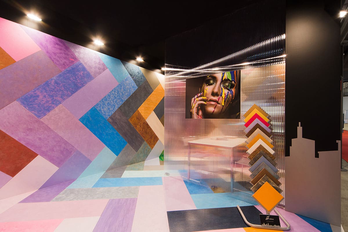 Allestimenti fieristici Madeexpo Milano casi reali: l' allestimento stand realizzato per Saber Color Srl visto dall' interno L' immagine raffigura un caso reale di allestimento fieristico: l' allestimento dello stand Saber Color realizzato da Diquadro in occasione di una precedente edizione della fiera Micam di Made Expo di Milano. L' immagine ci mostra l' interno dello stand nel quale sono esposte sia a parete che a pavimento le rifiniture colorate che produce l' azienda committente. L' allestimento dello stand è una vivacissima profusione di colori e superfici nella quale i visitatori possono immergersi.