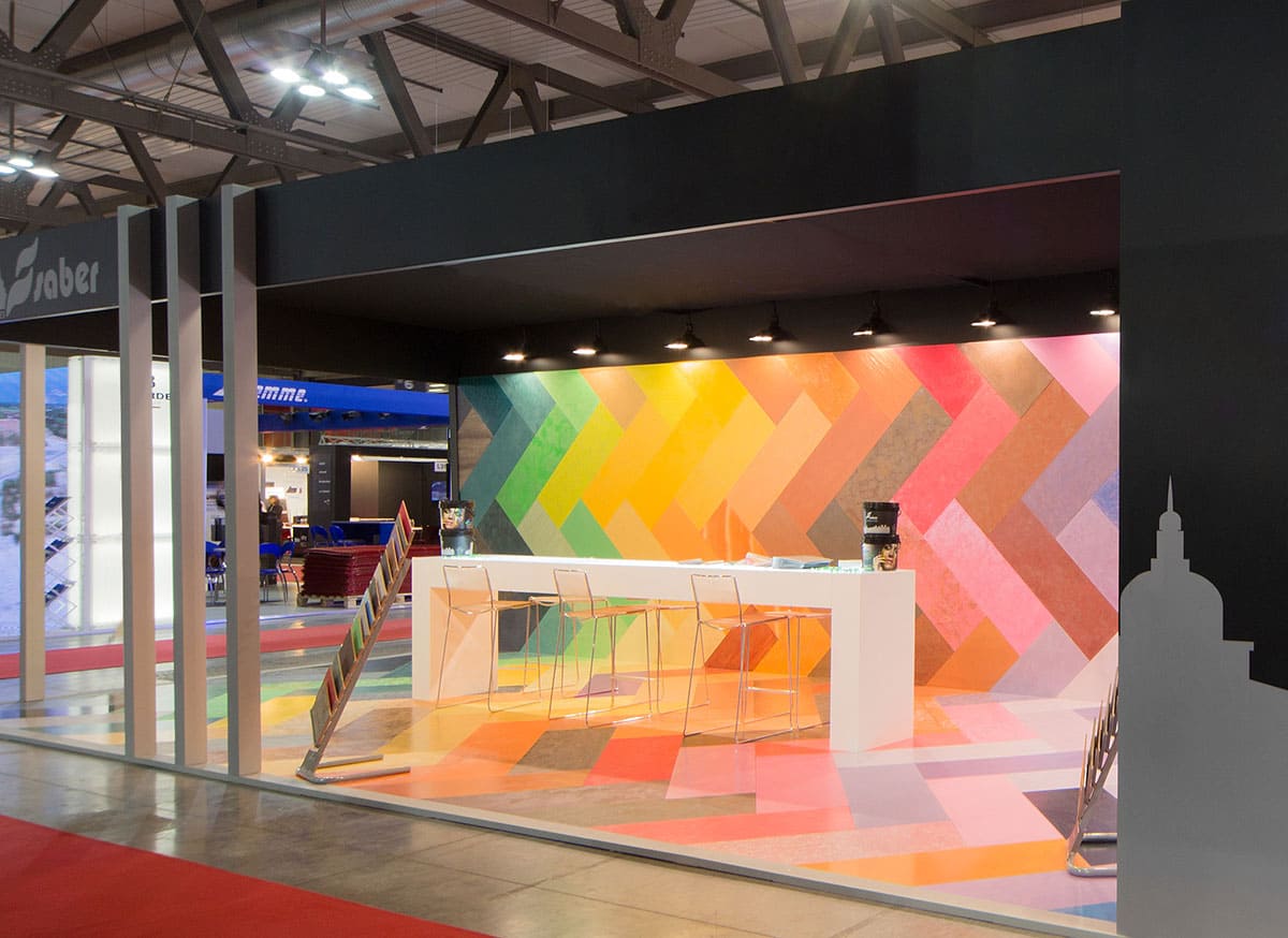 Allestimenti fieristici Madeexpo Milano casi reali: L'allestimento stand realizzato per Saber Color L'immagine raffigura un caso reale di allestimento fieristico: l'allestimento dello stand Saber Color realizzato per Made Expo di Milano. In particolare, nell'imagine si vedono due inquadrature. La prima a sinistra mostra un particolare dell'ingresso; la seconda a destra mostra un particolare di un'area espositiva.