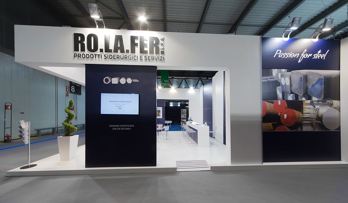 Come in precedenza, in questa foto è raffigurato il caso reale dell' allestimento stand Rolafer SpA realizzato da Diquadro allestitori fiere in occasione di una precedente edizione di Made in Steel di Milano. In questa foto, lo stand è è qui ripreso sul suo lato destro dove, oltre ad evidenziare la struttura principale che ha la forma di un estruso, sono sottolineati i vari elementi grafici: i loghi in acciao e le immagini fotografiche dei prodotti trattati da Rolafer.