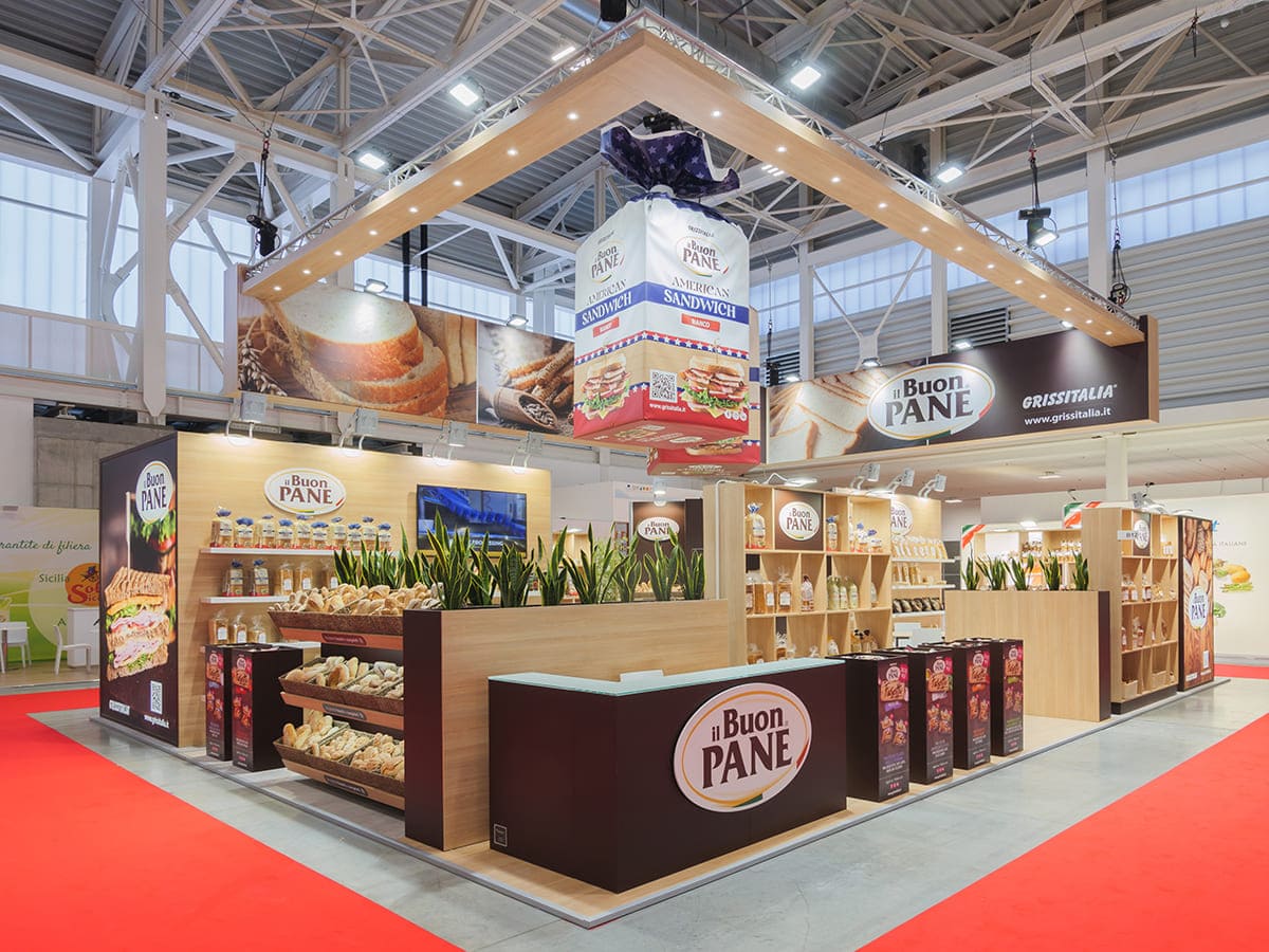 Allestimenti fieristici Marca Bologna casi reali: l' allestimento stand realizzato per Il Buon Pane Grissitalia Srl visto da Sud Ovest L' immagine raffigura un caso reale di allestimento fieristico: l' allestimento dello stand Grissitalia Srl che espone il marchio Il Buon Pane, realizzato da Diquadro in occasione di una precedente edizione delle fiera Marca di Bologna. L' immagine mostra una panoramica esterna dello stand da un' angolazione che sottolinea il punto di accoglienza ed i soprastanti mockup appesi.