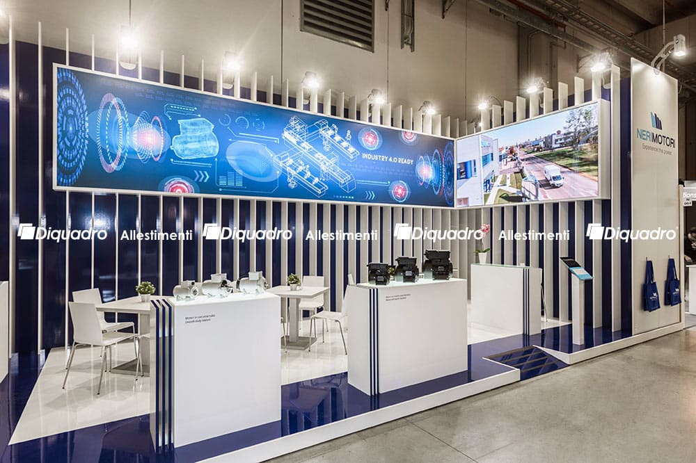 Allestimenti fieristici Mec Spe Parma casi reali: progetto di allestimento stand realizzato per Neri Motori Questa immagine raffigura il caso reale dell' allestimento fieristico Neri Motori allestito da Diquadro allestitori fiere in occasione di una precedente edizione di Mec Spe di Parma. L' immagine raffigura lo stand a distanza ravvicinata. Si notano la zona espositiva realizzata su piani retroilluminati per i prodotti Neri Motori, la zona incontri alle sue spalle e le pareti sul fondo lavorate ad elementi verticali, all' interno dei quali sono stati inseriti sia la grafica retroilluminata che il ledwall
