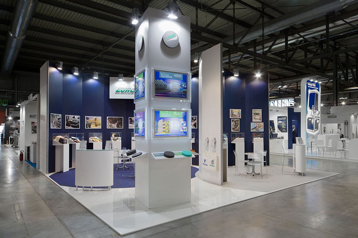 L' immagine raffigura un caso reale di allestimento fieristico: l' allestimento dello stand Eurofoam Technical Rubber realizzato in occasione di una precedente edizione della fiera Plast di Milano. La foto mostra una vista panoramica presa da Sud Ovest nella quale si notano le due pareti curve realizzate per suggerire lidea di sinergia e continuità tra le due aziende.