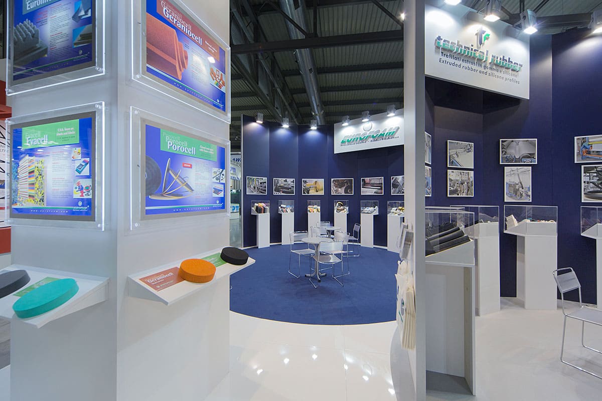 Come le alte fotografie di questo stand, questa immagine raffigura il caso reale dell' allestimento stand Eurofoam Technical Rubber realizzato da Diquadro allestitori fiere in occasione di una precedente edizione di Plast di Milano. Lo stand è è qui ripreso da un' angolazione che mostra l'interno Technical Rubber sullo sfondo dell'interno Eurofoam. Si notano le due zone espositive dello stand allestito per le due aziende e le lavorazioni effettuate al pavimento sui cambi di colore sagomati per sottolineare l'idea di collaborazione.